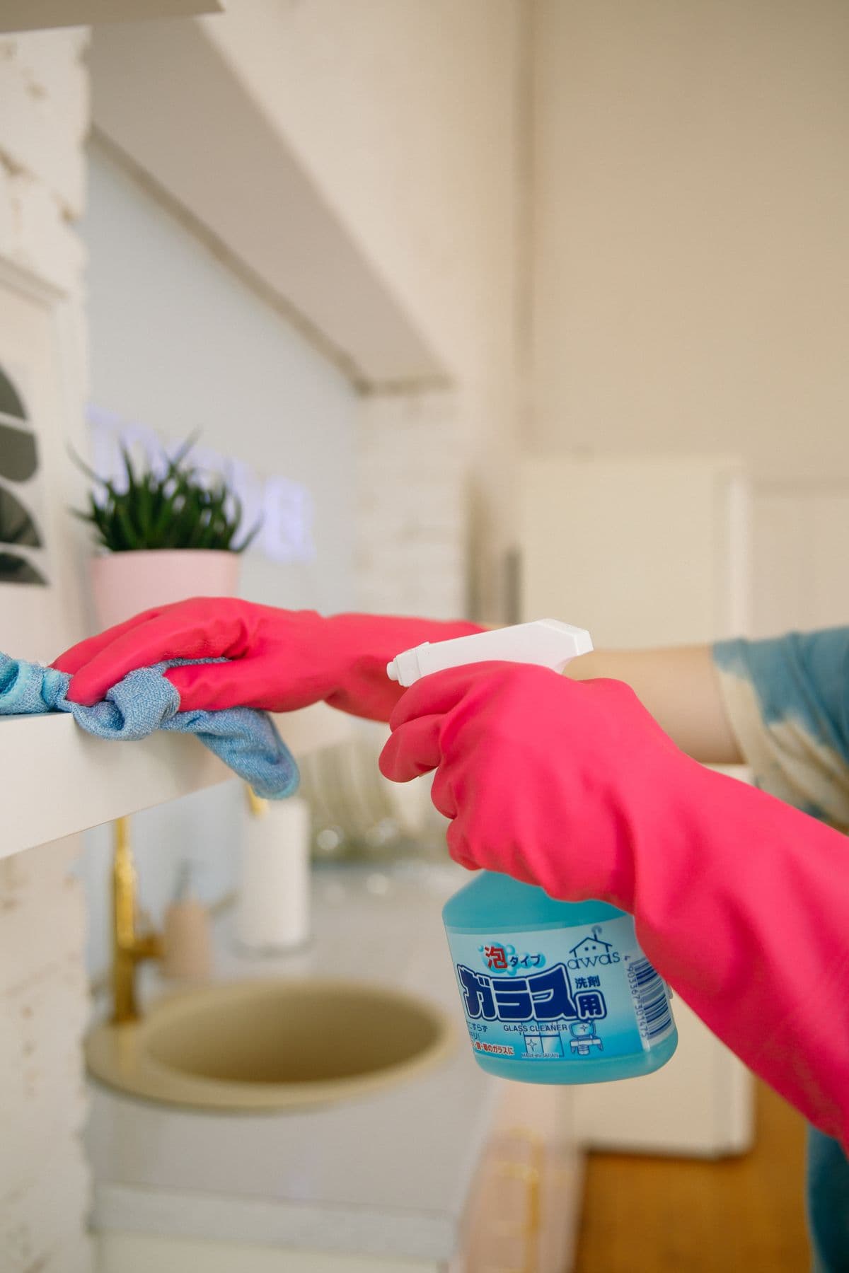Gloved hands wiping a shelf with a cloth and glass cleaner spray
