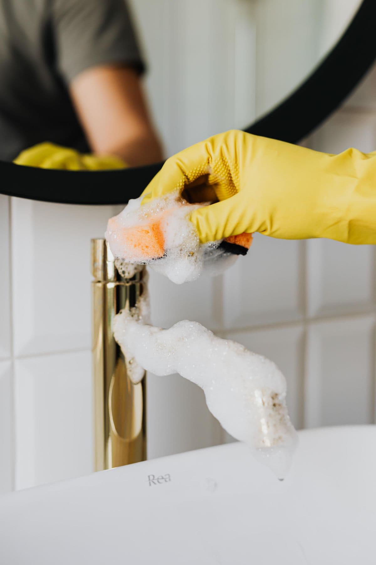 Hands in yellow gloves cleaning a sink tap
