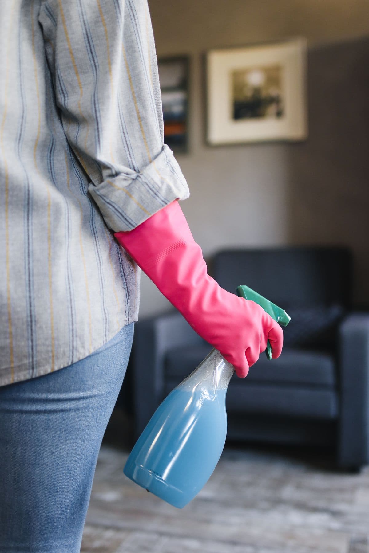Cleaner in a pink rubber glove holding a spray bottle in a living room