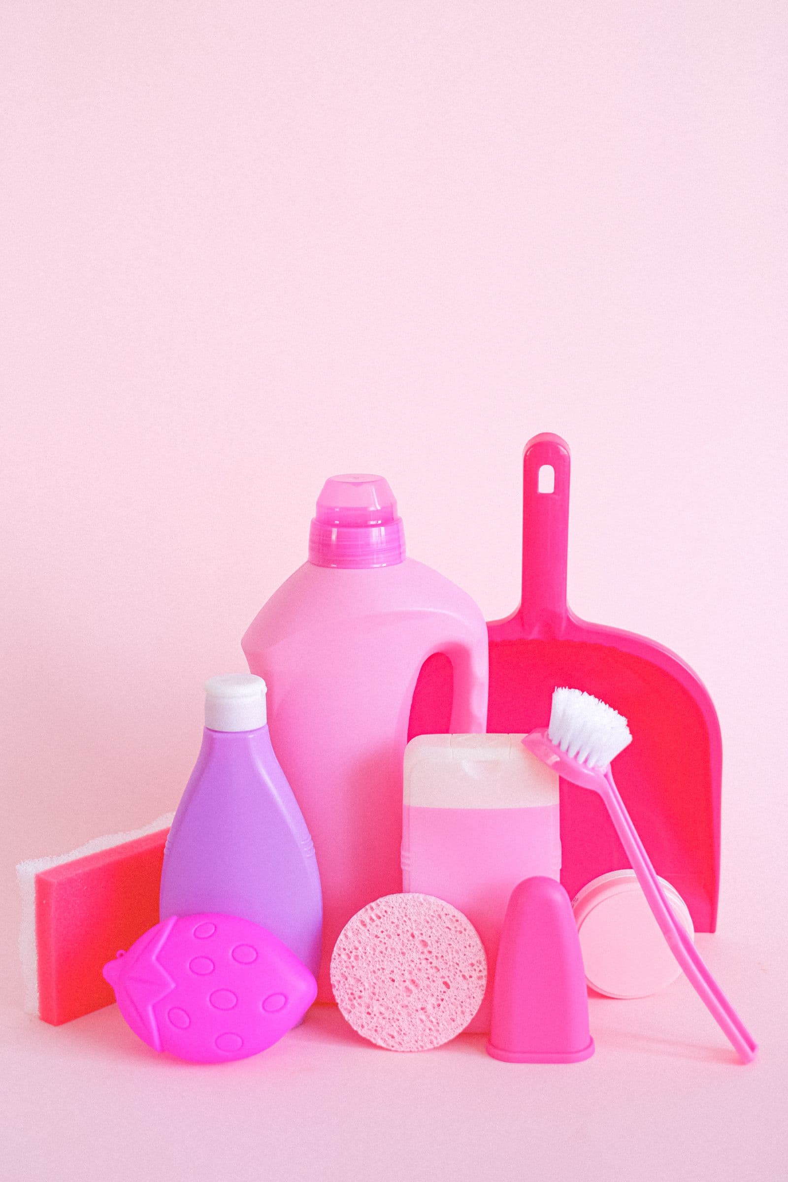 Cleaning bottles, sponge, brush and dustpan on a pink background
