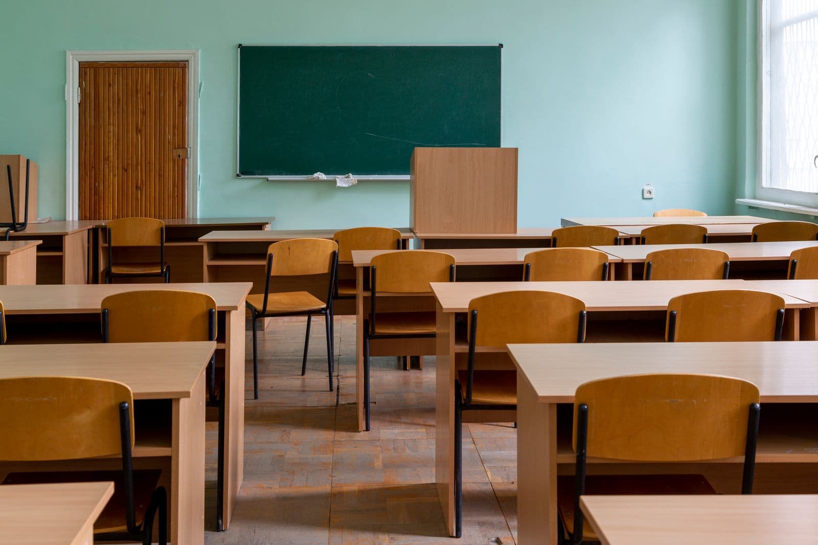Wooden desks and a green chalkboard in an empty classroom
